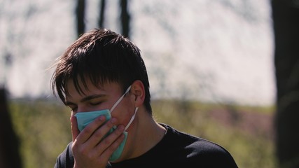 Close up of young Caucasian man taking on medical mask outdoor. Sick guy wearing protection during pandemic. Portrait of protected male. Healthcare concept.