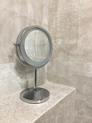 Round mirror on the leg in the bathroom. Porcelain wall background. Bathroom accessories, soap, towel, mirror.