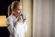 © JustLife - Beautiful woman drinking coffee in hotel room. Businesswoman working on lap top.