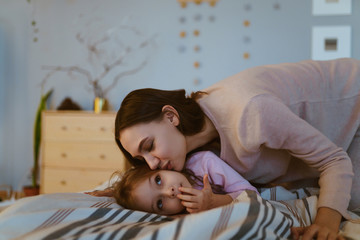 Wall Mural - mother kisses her daughter at night, she lies in the bed under the covers and looks thoughtfully at the ceiling