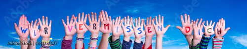 Children Hands Building Colorful German Word Wir Vermissen Dich Means We Miss You. Blue Sky As Background
