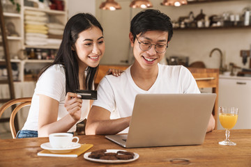 Poster - Image of happy couple holding credit card and using laptop