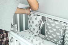 Father Helps Young Mother Put On Bumpers In The Crib. Family Lifestyle Concept