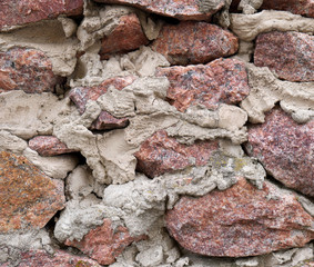 Wall of pink rough granite stone and cement mortar. Rubble masonry. Background texture for design.