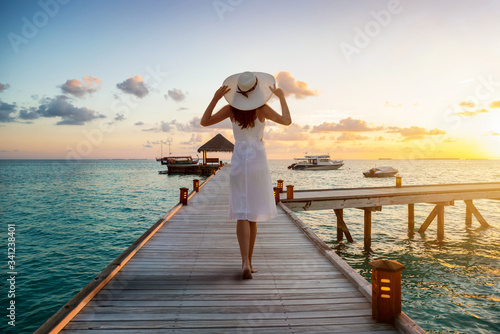 Fotografía A beautiful tourist woman in white dress on summer vacations walks over a wooden