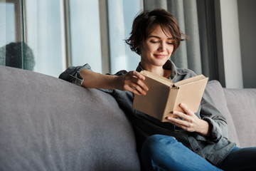 Sticker - Image of brunette cute focused woman reading book and smiling