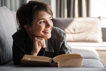 Canvas Print - Image of caucasian cute pleased woman reading book and smiling