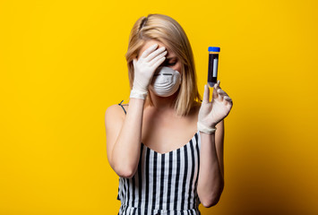 Blonde woman in face mask and gloves holds jar with blood