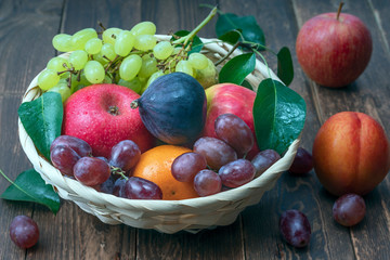 Wall Mural - red grape berries and fresh fruits in a straw basket on a dark wooden background.