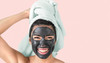 © Alessandro Biascioli - Happy smiling girl applying facial black mask - Young woman having skin care cleanser spa day - Beauty clean treatment and cosmetology products concept - Pink background