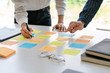 © snowing12 - Business people arranging sticky notes commenting and brainstorming on work priorities colleague in a modern co-working space.
