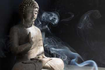 Buddha statue with smoke from aroma stick into sun light on black background stay calm home meditation anti stress yoga concept