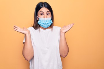 Poster - Young woman wearing protection mask for coronavirus disease over yellow background clueless and confused with open arms, no idea and doubtful face.