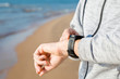 © fotoduets - Young man using smart watch for running on sea beach. Checking heart rate before and after workout. Monitoring of daily health with modern devices. Closeup.
