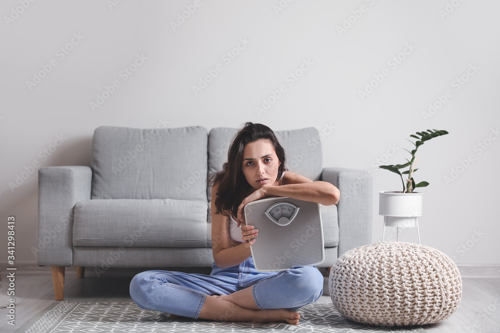 Young woman suffering from anorexia with scales at home