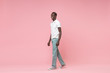 © ViDi Studio - Side view of smiling young african american man guy in white polo shirt, turquoise trousers posing isolated on pastel pink wall background. People lifestyle concept. Mock up copy space. Looking aside.