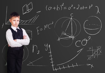 Little boy stands over blackboard background with formulas.