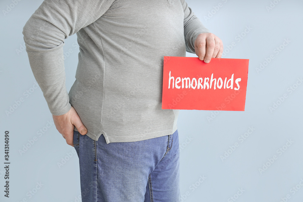 Elderly man holding paper with text HEMORRHOIDS on color background