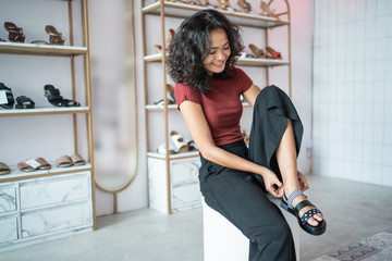 Wall Mural - portrait of beautiful asian woman try to put a shoes on while shopping in fashion boutique store. fitting customer