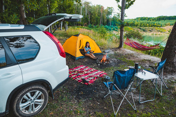 Wall Mural - camping near lake. woman sitting in yellow tent. white suv car