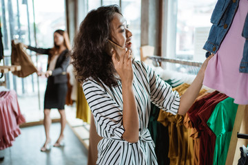 Wall Mural - beautiful young asian fashion shop owner at her boutique checking some product while making a phone call