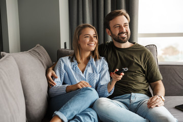 Wall Mural - Photo of joyful couple watching TV and using remote control