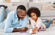 © Prostock-studio - Creative lockdown activities. African American girl and grandfather drawing with markers on floor in living room