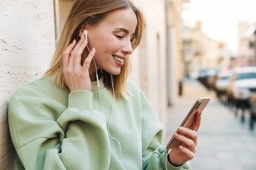 Sticker - Portrait of smiling young woman using earphones and mobile phone