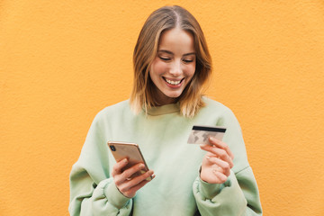 Wall Mural - Portrait of smiling woman holding credit card and using mobile phone