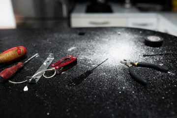 A set of tools for self-installation of the lamp lies on a black table, sprinkled with white dust. Husband for an hour. Household chores.