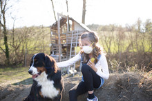 Girl Wearing Face Mask, Sitting In Garden, Playing With Her Dog