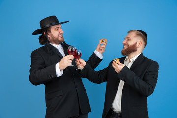 Dancing with wine, having fun. Portrait of a young orthodox jewish men isolated on blue studio background. Purim, business, festival, holiday, celebration Pesach or Passover, judaism, religion concept