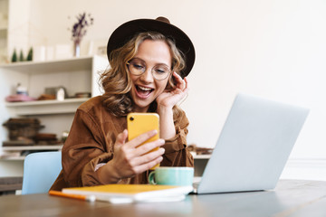 Canvas Print - Image of cheerful young woman working with laptop and mobile phone