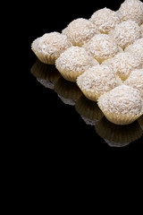 White coconut balls, raw and healthy sugar free rafaello candies on black glass background. Covering balls in coconut shred. Vegan, vegetarian sweets