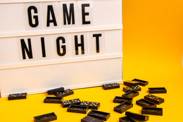 Game night text on lightbox with black dominoes on yellow background, table game