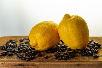 horizontal still life of two lemons on coffee beans.  White background with rustic wood table. 