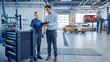 © Gorodenkoff - Car Service Manager and a Confident Female Mechanic Talk About Work Related Topics. They Use a Tablet Computer. Modern Clean Workshop with a Car on a Lift in the Background. Another Vehicle Drives In.
