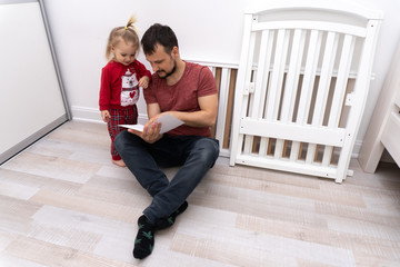 Cute baby help father to assemble cot, dad shows his child manual assembling the cradle