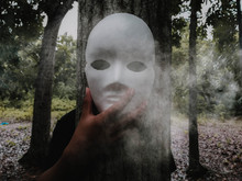 Man Wearing Mask While Standing By Tree Trunk In Forest