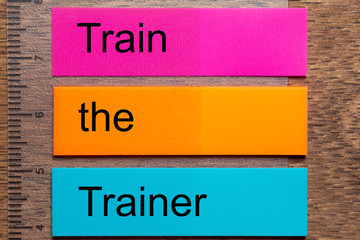 The words Train the Trainer are written on three stickers . A dark wooden table as a background