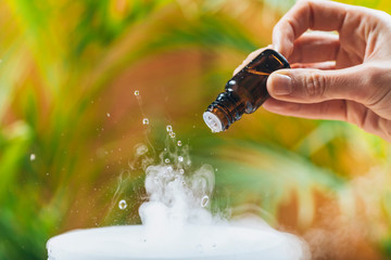 aromatherapy essential oil diffuser at home. female hand adding drops of aromatic essential oil into