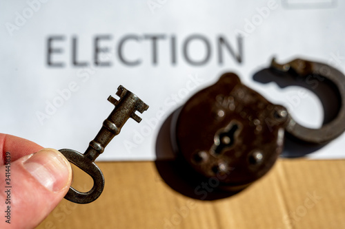 Hand holding a key in front of envelope for vote by mail ballot depicting the key to election security.  Selective focus
