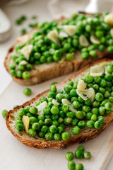 Wall Mural - Sourdough bread sandwiches with stewed green peas, olive oil and garlic on a white wooden board close up 