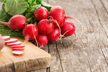 Harvested bunch of fresh raw red radishes with leaf near cutting board on sliced radish. Healthy organic vegetable ( Raphanus sativus )