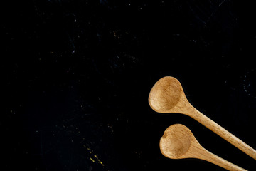 Top view of two wooden kitchen spoons in a black wooden cooking table