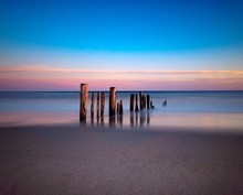 Wooden Posts At Beach Against Sky During Sunset