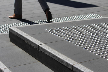 Man legs stepping down from steps. The steps have stainless steel tactile indicator studs that have been installed in a grid formation. The tactile studs are also at the base of the stair. Australia