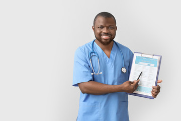 African-American doctor with clipboard on light background