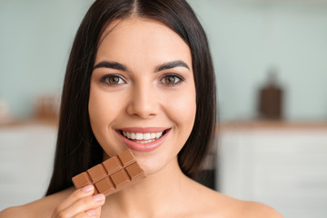 Wall Mural - Beautiful young woman eating chocolate in kitchen