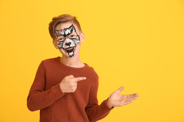 Canvas Print - Funny little boy with face painting pointing at something on color background